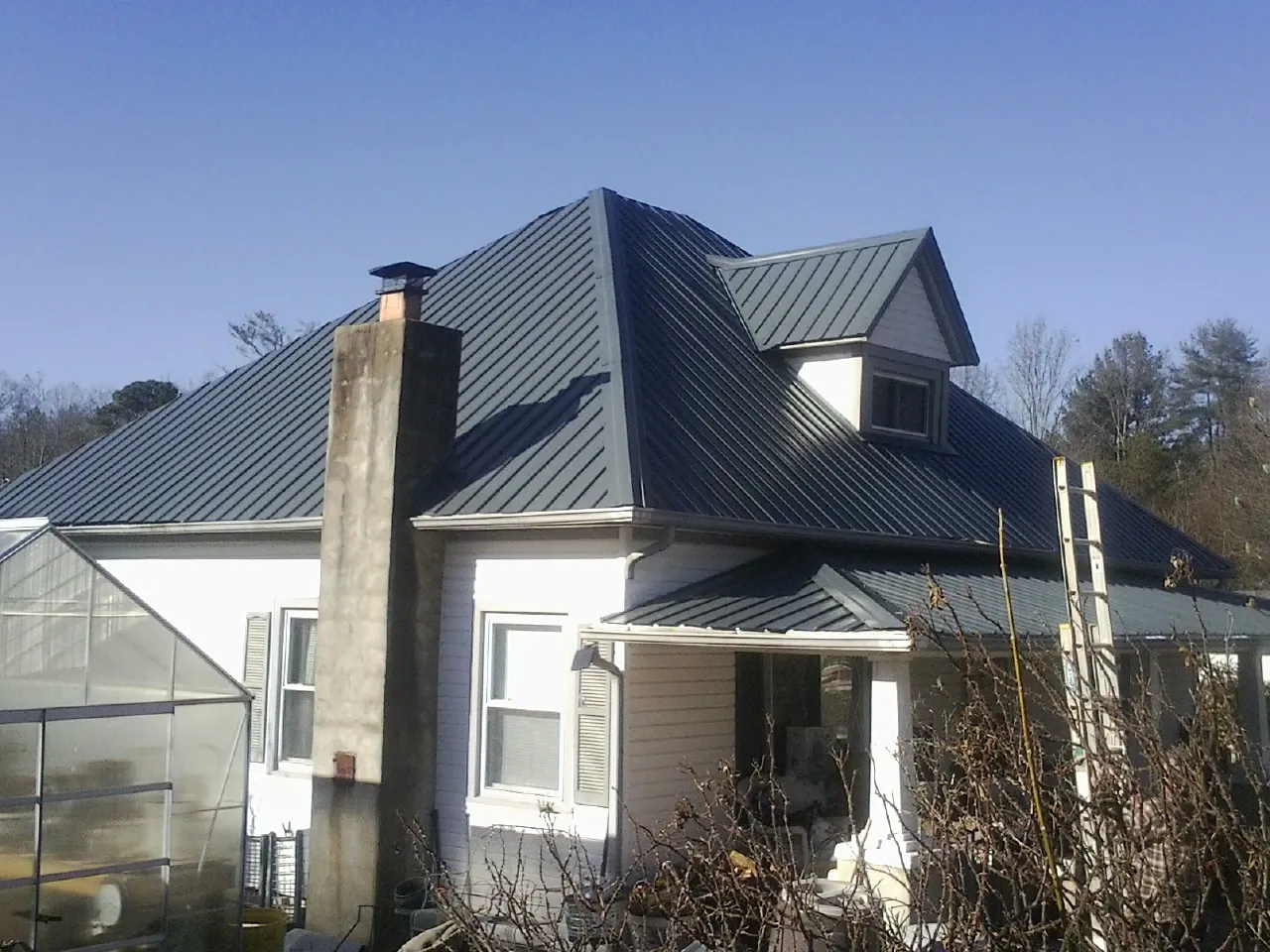 Dark blue standing seam metal roof on a white farmhouse with dormer — Slate & Tile Roof Repair by Roofing Brothers in Wynantskill