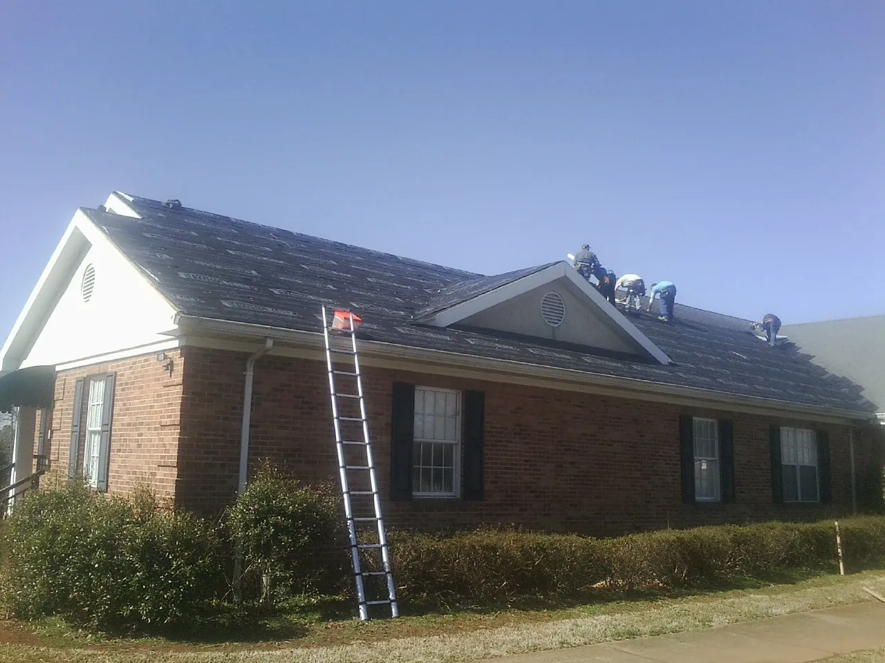Crew tearing shingles off a brick ranch roof with a ladder set — Emergency Roof Repair work by our crew in Wynantskill