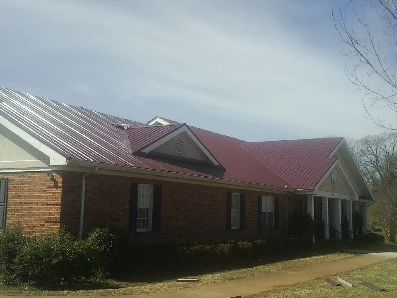 Red metal roof with gabled entries on a long brick building, from a Hail Damage Roof Repair job in Wynantskill