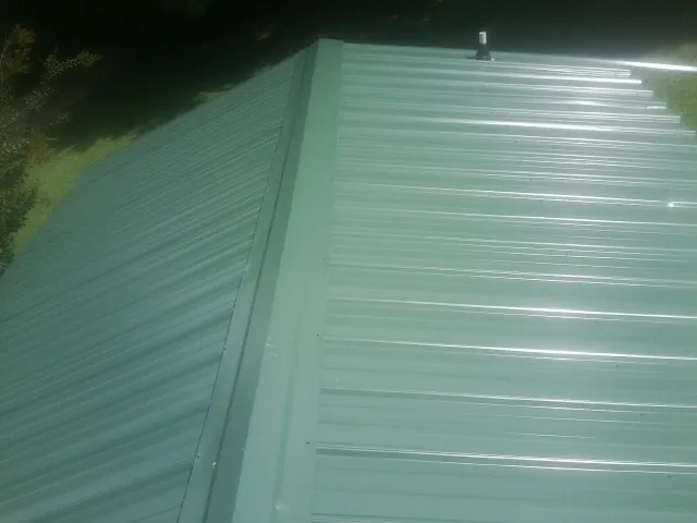 New green metal panels meeting at the ridge of a roof — Flat Roof Repair work by our crew in Wynantskill