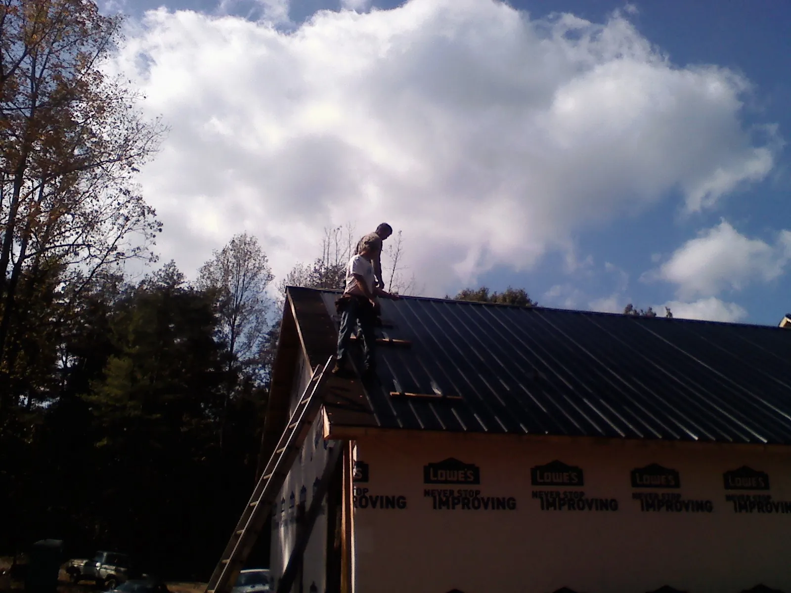 Roofer fastening dark metal panels high against a cloudy sky, from a Roof Inspection job in Wynantskill