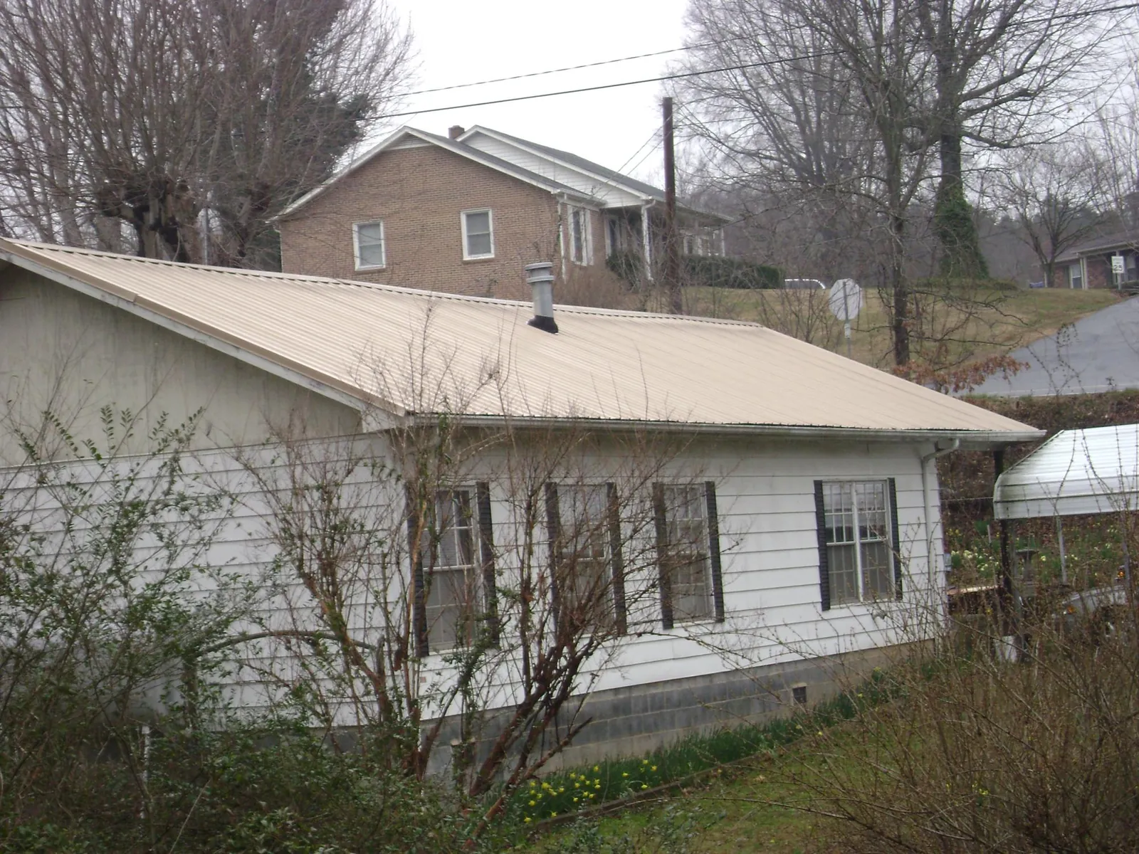 Tan metal roof on a white sided house set into a hillside — Commercial Roofing by Roofing Brothers in Wynantskill