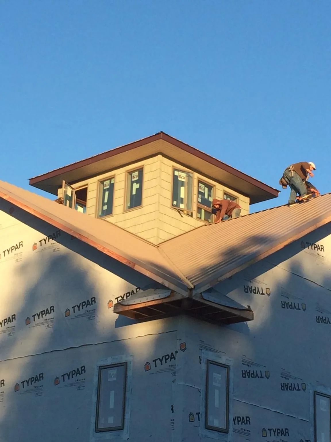 Roofers working around a rooftop cupola on a new metal roof at sunset — Roof Waterproofing in Wynantskill by Roofing Brothers